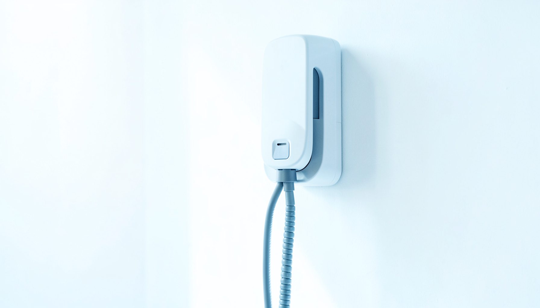 Bright, airy photograph of a sleek wall-mounted EV charging station with a coiled cable, modern industrial design, set against a clean white wall