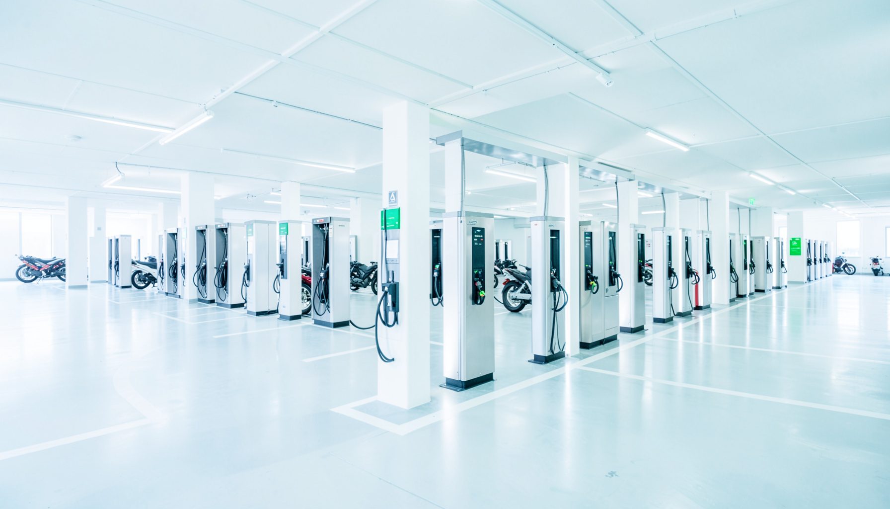 Rows of electric vehicle charging stations in a bright modern parking facility, clean white and silver tones with green accents